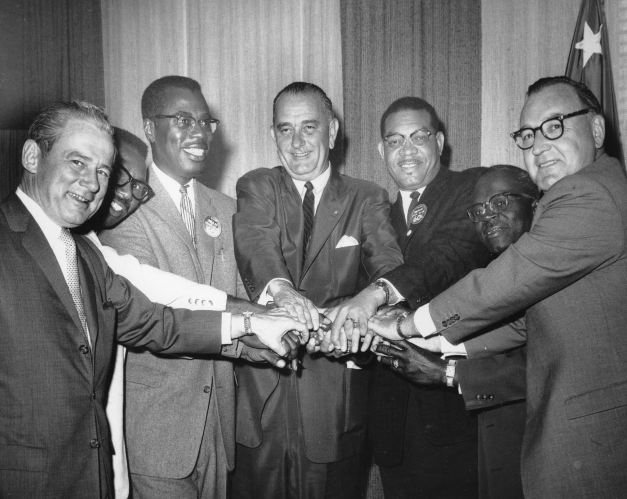 Group of men, including Nathaniel Colley and Lyndon B. Johnson, in a semi-circle with their hands in the middle.
