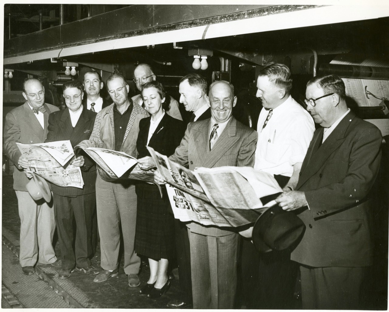 Men standing in a line, reading the newspaper