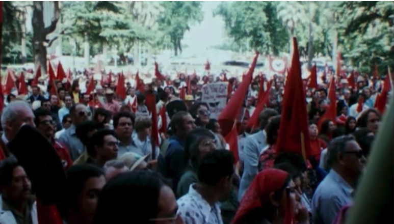 A crowd gathers outside with red flags