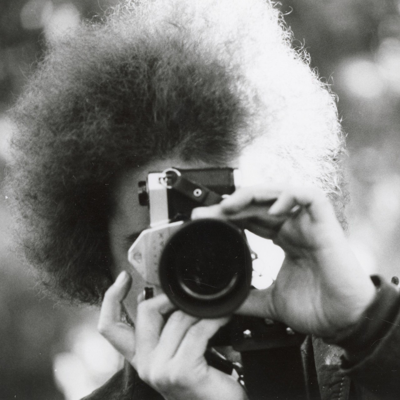Black and white photo of Linda Birner behind the lens of a camera about to take a photo.