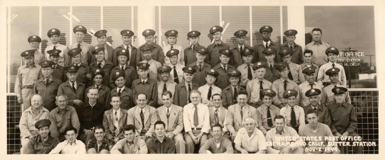 Postal service workers pose in front of a post office